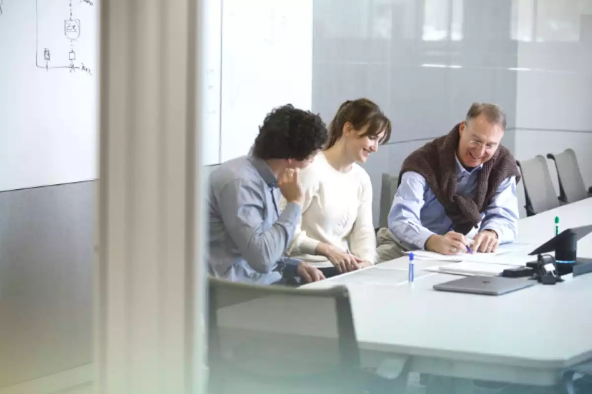 Three people sit around a conference room table and work together.