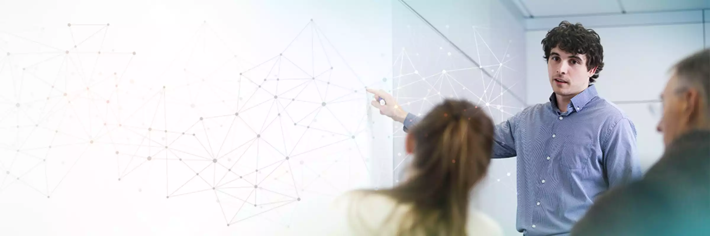 A man explains a concept on a white board to two colleagues.